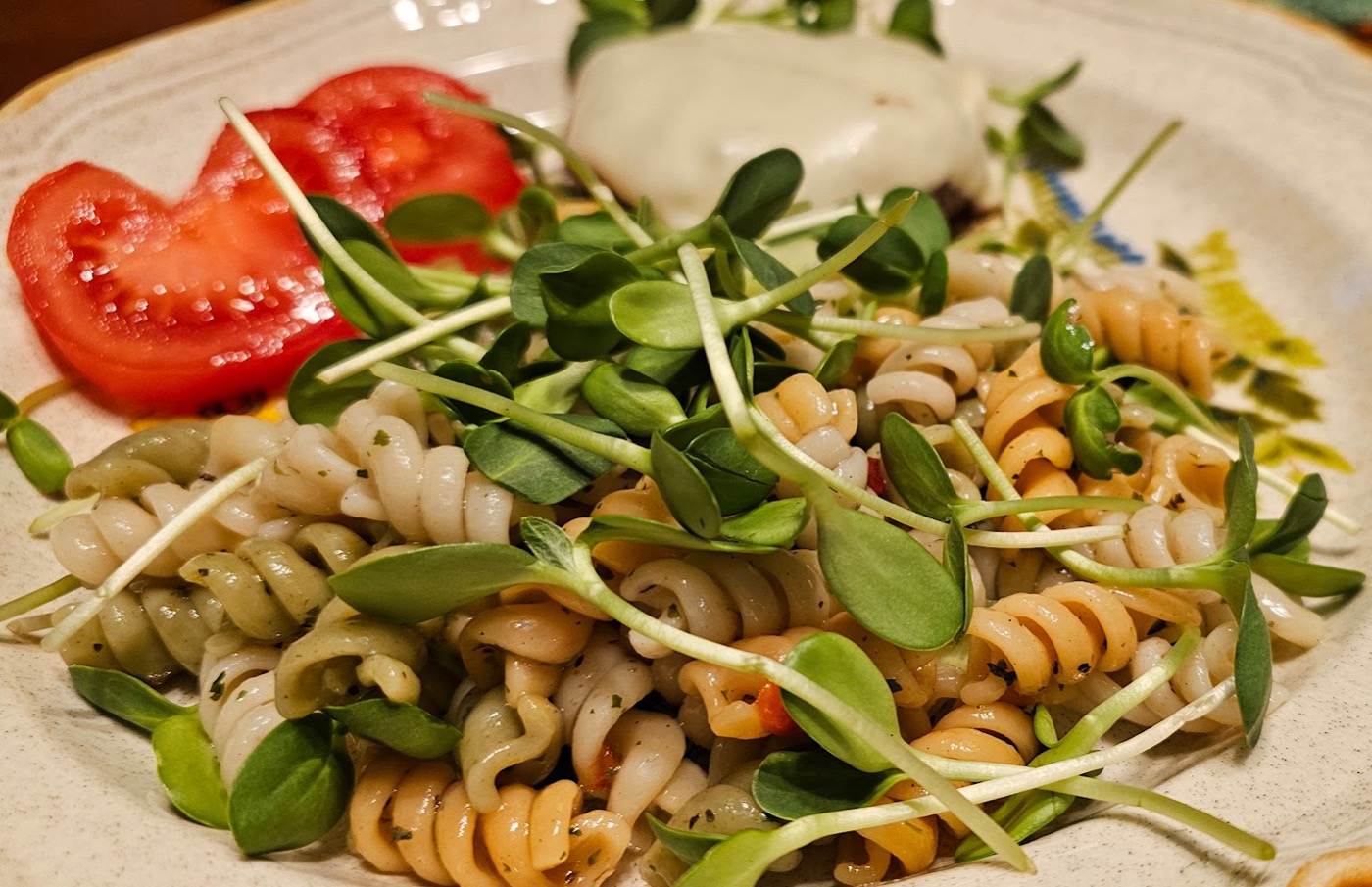 Pasta dish garnished with sunflower microgreens alongside fresh tomatoes and dip